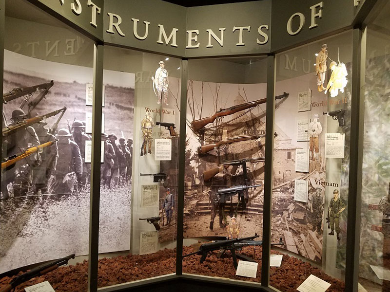 US Army museum display of several firearms in glass enclosure.